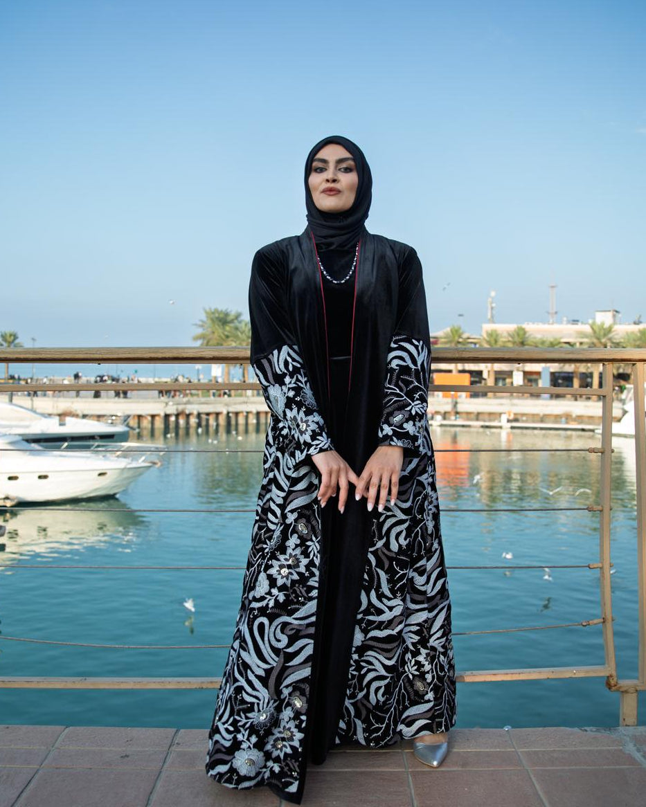 Woman in a black and white patterned abaya standing by a marina.
